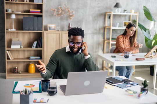 Happy black man talking on phone in modern office