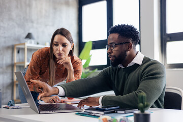 Coworkers collaborating on laptop pointing at screen in office