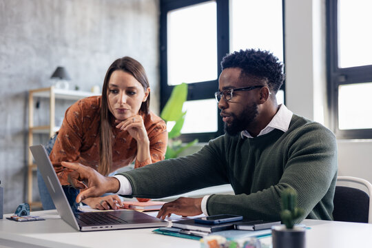 Coworkers collaborating on laptop pointing at screen in office