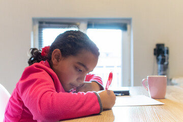 Young mixed race girl concentrating on doing homework, practicing writing, learning new skills, and developing her focus at a desk at home