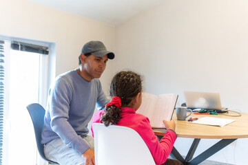 Father helping his young daughter with homework, supporting her learning and academic development, sitting together in a focused home study environment