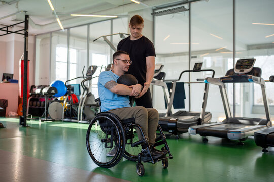 Disabled man practice controlled exercised with medicine ball, rotational and one sided lifts under supervision. Therapeutic workout, inclusive upper body sports, trainer support rehabilitation - Powered by Adobe