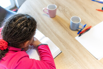 Young girl learning, concentrating on an open book during a study session at home, showing dedication in early childhood education and academic development