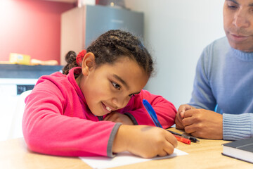 Young girl learning and developing her skills at home, her father supervising and supporting her while focusing on homework or creative activity