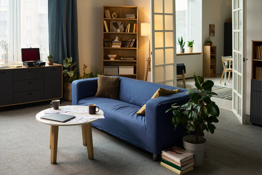 Modern living room featuring round table with laptop, documents, calculator and coffee cups suggesting tax preparation or financial planning in comfortable home environment