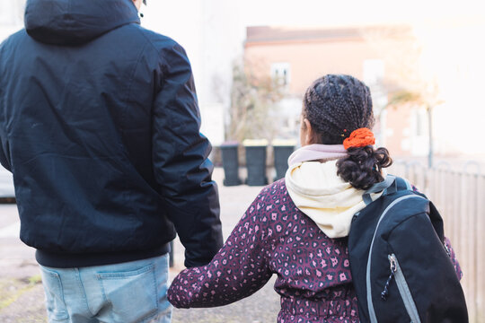 Grandfather holding granddaughter's hand, walking outdoors, providing guidance and support for the child's educational journey and future, symbolizing family bond