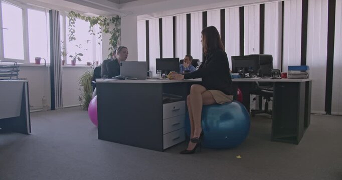 Business colleagues discuss work in a modern office. They sit on exercise balls for active sitting and posture support.