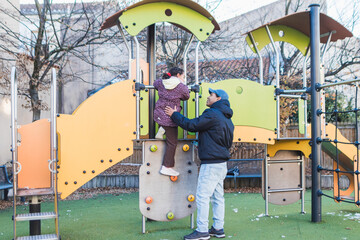 Father helping young daughter climb rock wall on playful outdoor playground structure, depicting childhood development, family bonding, and parenting support