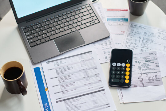 Closeup of financial documents, calculator, laptop and coffee cup on table showing tax forms and utility bills, illustrating process of calculating and paying taxes at home or office