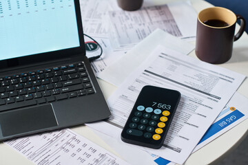Closeup of smartphone with calculator app, laptop, coffee mug and assorted financial documents...