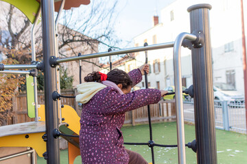 Child with braided hair is climbing a rope net structure in an outdoor playground, engaging in...
