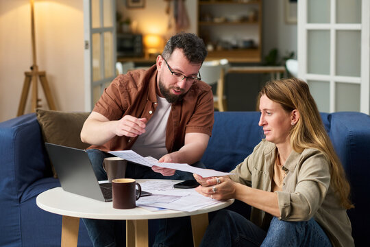 Caucasian middle aged man and Caucasian middle aged woman sitting at table reviewing financial documents and using laptop