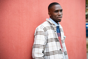 Stylish young man poses confidently against a vibrant red wall outdoors in the afternoon