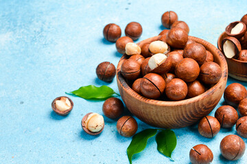 Macadamia nuts in a bowl on a blue stone background. Close-up, side view.