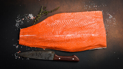Half raw salmon or trout fillet on dark stone surface. Top view.