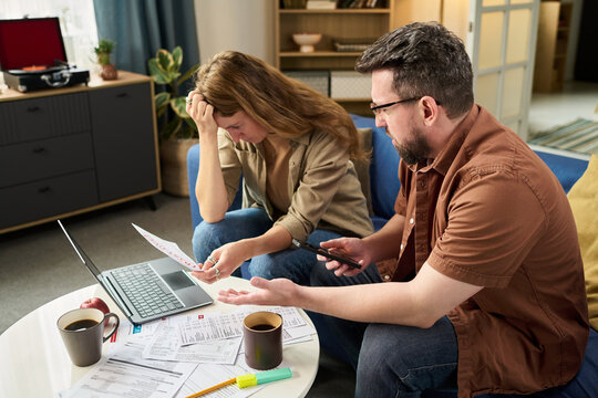 Caucasian young woman and Caucasian young man sitting at table reviewing tax documents and using laptop, both appearing stressed while discussing financial paperwork and deadlines - Powered by Adobe