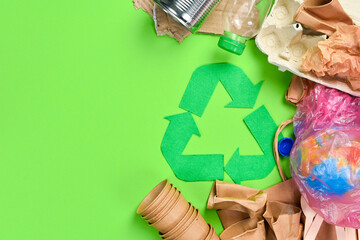 Green background with recycling symbol. Flat lay of various types of garbage. Top view.