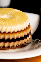 Extreme close-up of a layered chocolate and vanilla agar-agar pudding, revealing the glossy ribbed texture and intricate striped layers on a white plate with a fork nearby.