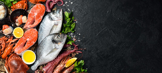 Black slate stone background with seafood. Fish, clams, scallops, octopus, lobster and other seafood on the table. Free copy space.