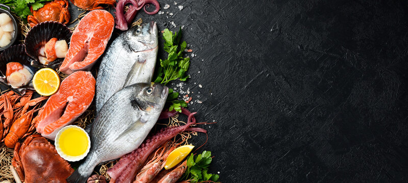Black slate stone background with seafood. Fish, clams, scallops, octopus, lobster and other seafood on the table. Free copy space.
