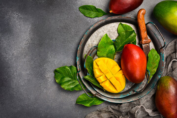 Fresh mango slices and ripe whole mango fruits on a plate. Top view. Fresh tropical fruits.