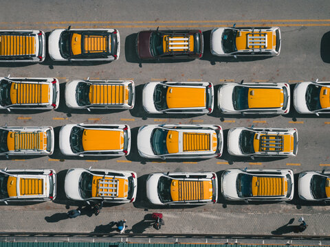 Aerial view of neatly arranged cars with vibrant yellow tops contrast against the stark grey asphalt, creating a rhythmic pattern from above, Thimphu, Bhutan.