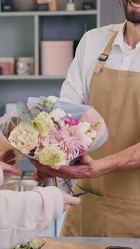 Woman buys flowers and pays with credit card using terminal. Male florist sells a beautiful bouquet to customer. Modern flower shop small business.