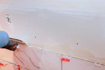 Workers are applying tile adhesive using spacers for precise alignment during bathroom renovation.