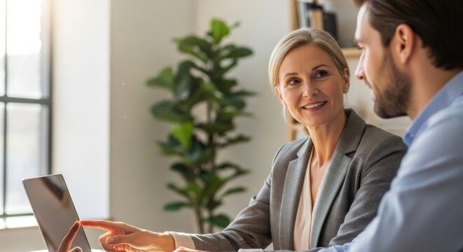 Businesswoman and businessman reviewing data on a tablet in a bright modern office with a plant in the background