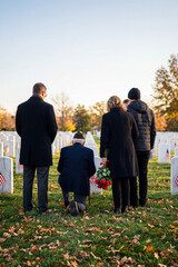 A group of people, including a veteran kneeling, pay their respects at a military cemetery adorned with small American flags.