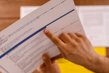 Fototapeta premium Close-up of a hand pointing at code on paper, suggesting a technical or analytical context. Focus on software development or information.