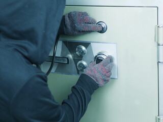 A thief wearing gloves is trying to open a safe.