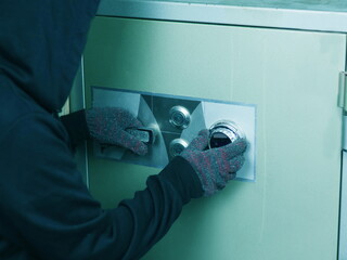 Gloved hand of a thief attempting to open a metal safe.