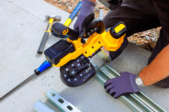 Worker uses an handheld electric saw cutting metal framing while constructing new building
