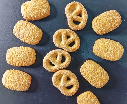 Scattered Danish butter cookies on a dark surface. Overhead view of assorted golden shortbread biscuits, including pretzel and rectangle shapes, perfect for sweet dessert backgrounds, holiday concept.