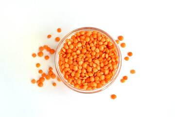 Red lentil groats lie in and around a glass bowl.