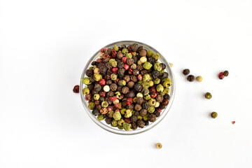 Different colored peppercorns in and around a glass bowl.
