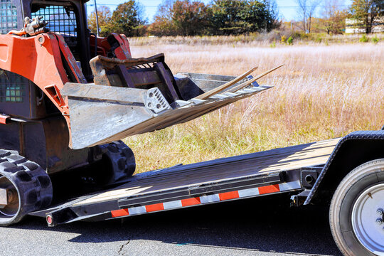 An skid steer is unloading on flatbed trailer at construction site