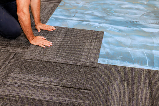 Skilled worker lays gray carpet tiles in an office area to create stylish functional workspace