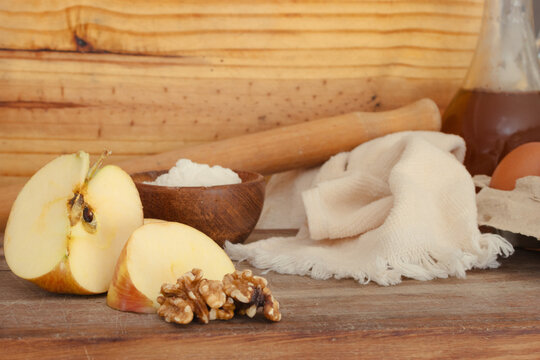 Rustic wooden table with baking ingredients for apple walnut desserts, sliced apples, walnuts, flour, eggs, oil, rolling pin and towel ready for homemade pies and pastries