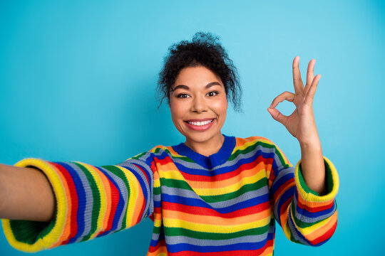Young woman smiling in a rainbow striped sweater standing against blue background ideal for fashion lifestyle advertising and diverse inclusive campaigns