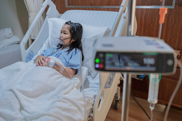 Sick Asian girl wearing oxygen mask lying on hospital bed receiving treatment. Healthcare concept, respiratory disease, hospital admission, medical care, and child patient in emergency situation.
