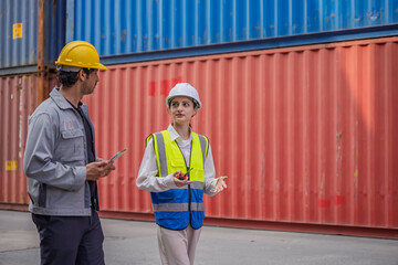 Professional logistics engineers walking and discussing operations at a cargo terminal. Female supervisor communicating with a male colleague holding a digital tablet during shipping inspection.