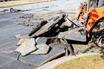 Construction skid steer is clearing debris from damaged pavement during road repair © ungvar