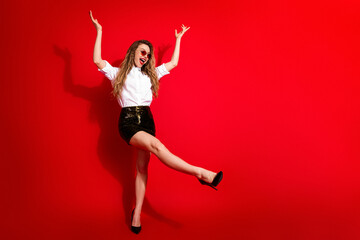 Excited young woman raising her arms in celebration on a vibrant red background, exuding happiness