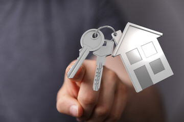 Person hand holding house keys with home shaped pendant, represents the purchase of a home, new...