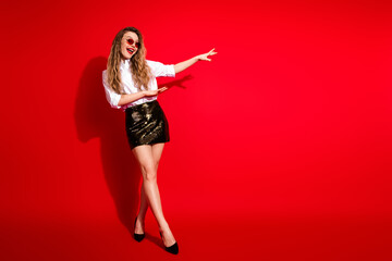 Stylish young woman in formalwear pointing with a cheerful expression against a vibrant red...