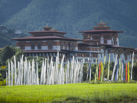 Aerial view of the majestic Punakha Dzong rises with vibrant prayer flags fluttering against the backdrop of lush greenery, Punakha, Punakha, Bhutan.