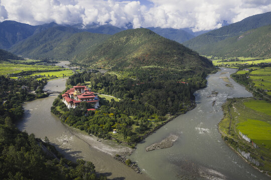 Aerial view of the majestic Punakha Dzong standing resiliently at the confluence of two rivers, framed by verdant hills under a sky of scattered clouds, Punakha Dzong, Punakha, Bhutan.