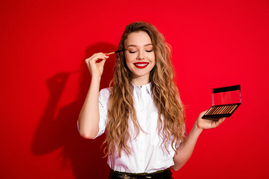 Beautiful woman applying makeup using an eyeshadow palette against a vibrant red background showcasing elegance and style